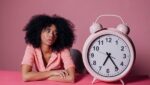 real estate broker looking at a pink alarm clock wondering how long it takes to recruit real estate agents to her brokerage