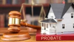 An image depicting probate real estate. A white model house on a red book marked Probate next to a Judge's probate court hammer depicting a realtor selling Probate property.