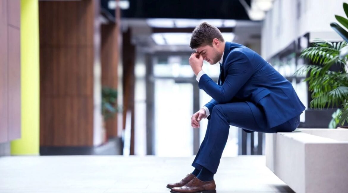 real estate recruiter fail and now sitting looking sad in the hallway on a bench wearing a blue suit and brown shoes.
